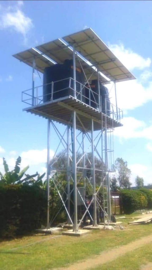 elevated steel stand wit two 10,000 liter tanks and solar panels above  